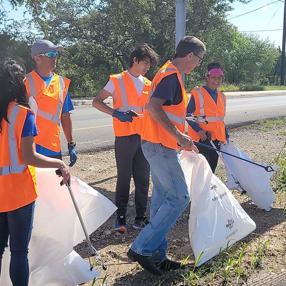 A group of people in orange vests holding trash bags.